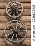 Two old wheels of different diameters from a cart fixed on a log wall