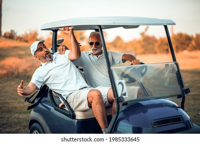 Two Older Friends Are Riding In A Golf Cart.