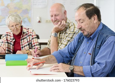 Two Older Men And One Woman Sitting At A Table Taking Notes.