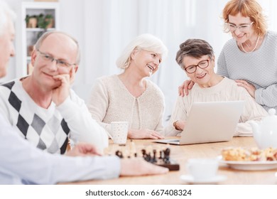 Two older men playing chess and three senior women using laptop
