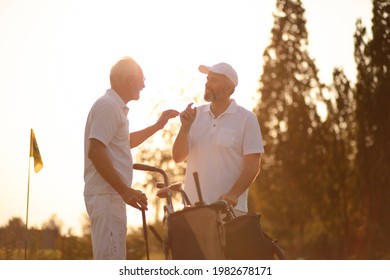 Two Older Men Stand On A Golf Course And Talk. 