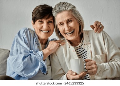 Two older women, a loving mature lesbian couple, sit together on a couch, enjoying a cup of coffee. - Powered by Shutterstock