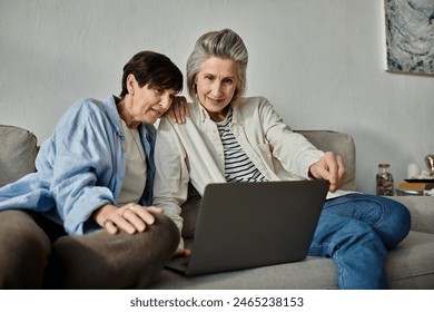 Two older women, a loving mature lesbian couple, sit on a couch, engrossed in a laptop. - Powered by Shutterstock