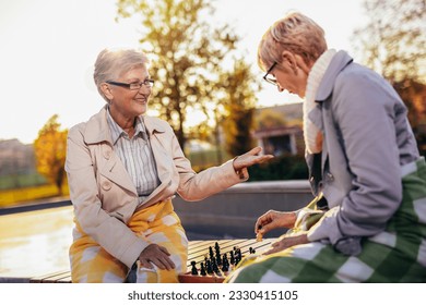 Two older women playing chess and having fun with it in the colorful park in the autumn - Powered by Shutterstock