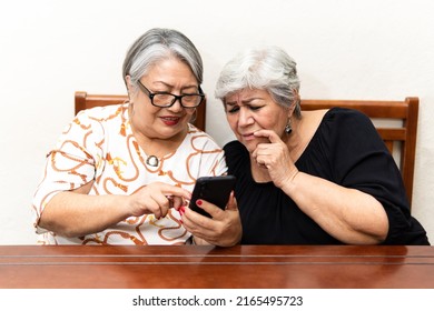 Two Older Women Watching News On Cell Phones, Making Faces At The Lack Of Glasses. 