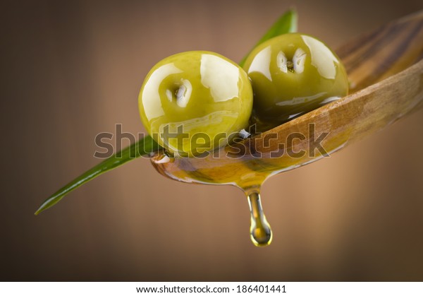 Two olives\
and leaves with drop oil on wood spoon\
