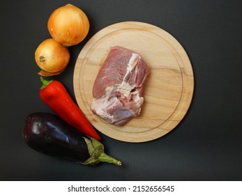 Two Onions, Pepper, Eggplant And Pork Fillet On A Cutting Board On A Black Background, View From Above