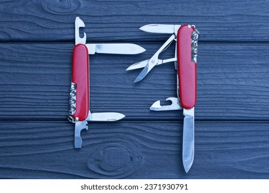 two open folding knives multitools with red handles with gray blades lie on a black wooden table