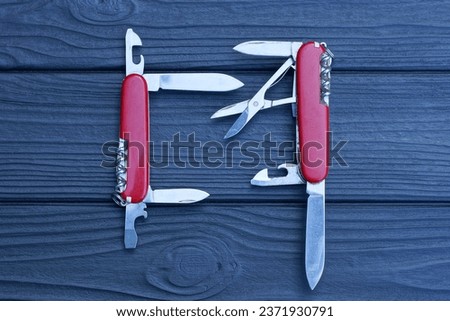 two open folding knives multitools with red handles with gray blades lie on a black wooden table
