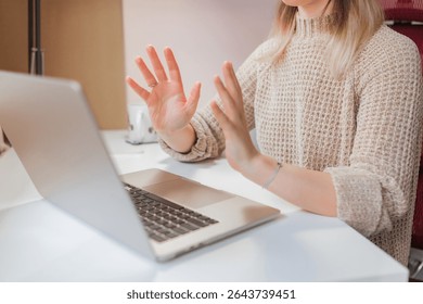 Two open palms facing screen, woman speaks using expressive hand gestures during online call, casual home setup with mug and notebook visible.Woman holds up hands while communicating during remote
