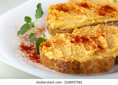 Two Open Sandwiches With Hummus And Paprika Powder On A White Plate