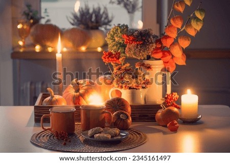 two orange cups  of tea and autumn decor with pumpkins, flowers and burning candles on table