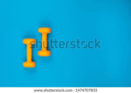 Two orange dumbbells on blue background, shot from above, aligned to the left.