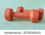 Two orange dumbbells on a green background. Fitness concept.