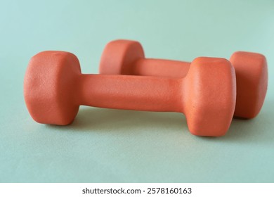 Two orange dumbbells on a green background. Fitness concept.