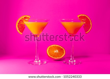two orange juice glasses with orange slice on pink background