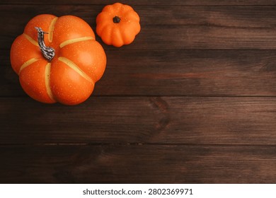 Two orange pumpkins sit on a wooden table in preparation for autumn. The larger pumpkin has a shiny surface while the smaller one adds to the seasonal feel.
