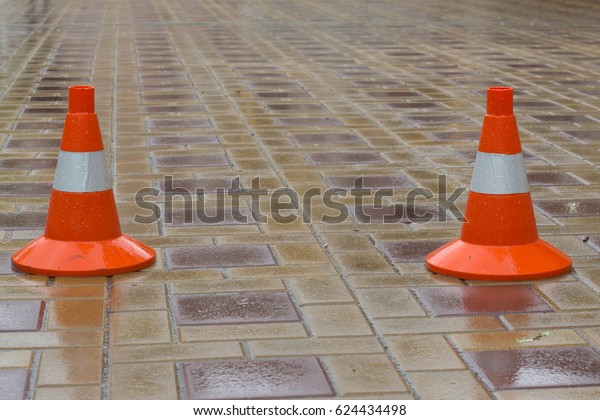 Two orange road cones on the paving slab. Block\
the traffic