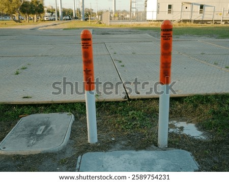 Two orange and white underground utility marker poles in front of temporary road access mats low angle view across the grass for Protection from heavy loads. Late afternoon sun in Florida. Wide view