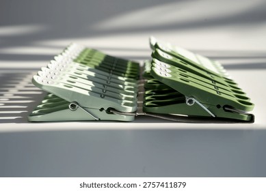 Two organized rows of spring-loaded plastic clothespins in different shades of green casting striped shadows, representing household chores and laundry