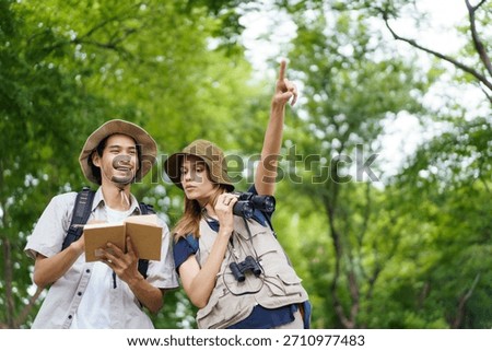 Two outdoor explorers study their surroundings in forest, using notebook and binoculars while discussing their route. Adventure and nature exploration in peaceful woodland environment. Bird watching.