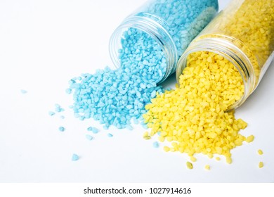 Two overturned jars with small pebbles, yellow and turquoise. Spilled pebbles on a white table.