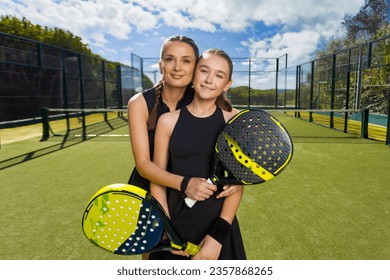 Two padel tennis players with rackets. Woman and girl teenager athlete with paddle racket on court outdoors. Sport concept. Download a high quality photo for the design of a sports app or web site. - Powered by Shutterstock