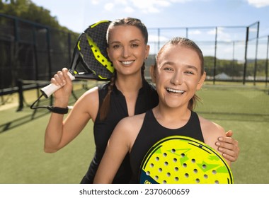 Two padel tennis players with rackets. Woman and girl teenager athlete with paddle racket on court outdoors. Sport concept. Download a high quality photo for the design of a sports app or web site. - Powered by Shutterstock