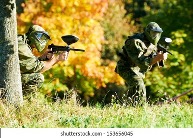 Two paintball sport players in prootective uniform and mask aiming and shoting with gun outdoors