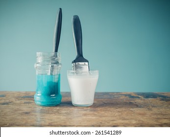 Two paintbrushes are soaking in jars of water and are coloring the water white and blue - Powered by Shutterstock
