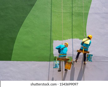 Two painters are painting the exterior of the building on a dangerous looking scaffolding hanging from a tall building with copy space.