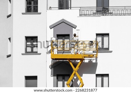 Two painters painting the facade of the building with paint rollers from the lift cradle