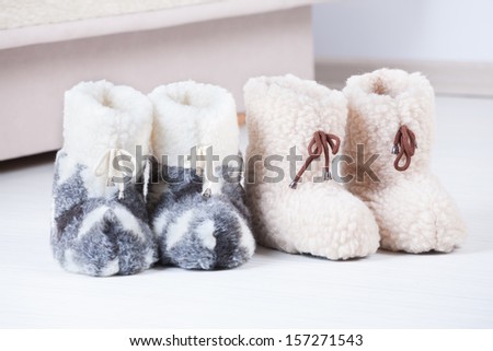 Two pair of natural woollen slippers on wooden floor