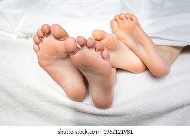 Two pairs of baby legs protrude from under the covers on the bed - Shutterstock ID 1962121981