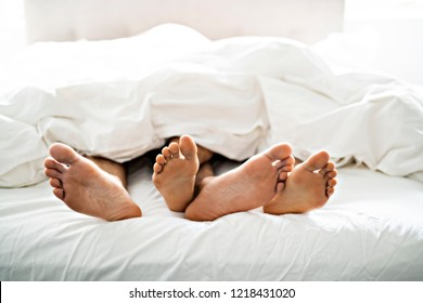 Two Pairs Of Feet Under Duvet Couple Makes Love In Bed