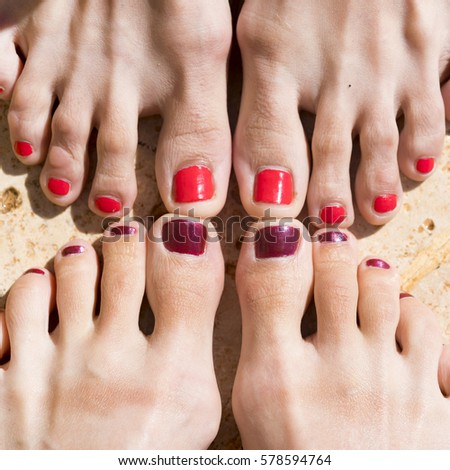 Two pairs of female feet with red nail polish on the sand