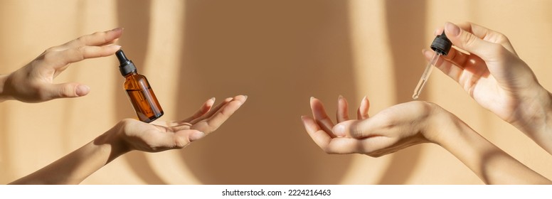 Two pairs of female hands hold bottle of amber glass with cosmetic serum and pipette with moisturizing oil on light brown background, in rays of sunlight. Close-up, banner. Mockup concept - Powered by Shutterstock