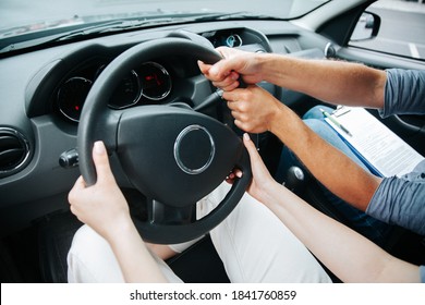 Two Pairs Of Hands Turn Steering Wheel Together. Female Student At Driving Courses Hold The Wheel And Male Instructor Helps Her To Drive. Driving Lessons Concept. Close Up View.