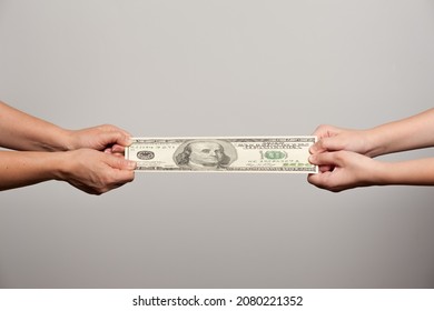two pairs of human hands stretching a hundred dollar bill