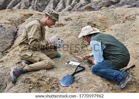 two paleontologists extract fossilized remains from the ground in the desert