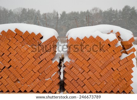 two pallets of brick blocks stored outdoors, with snow falling on top and with distant forest background