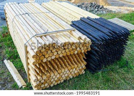 two pallets with long round natural wooden fence posts with tarred and sharpened ends