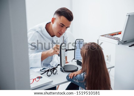 Two panels on the table. Young ophthalmologist is with little female visitor in the clinic.