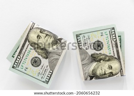 Two paper bills with a face value of one hundred dollars, folded in half, on a white background. Close-up