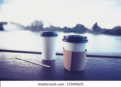 Two Paper Coffee Cups By A Lake