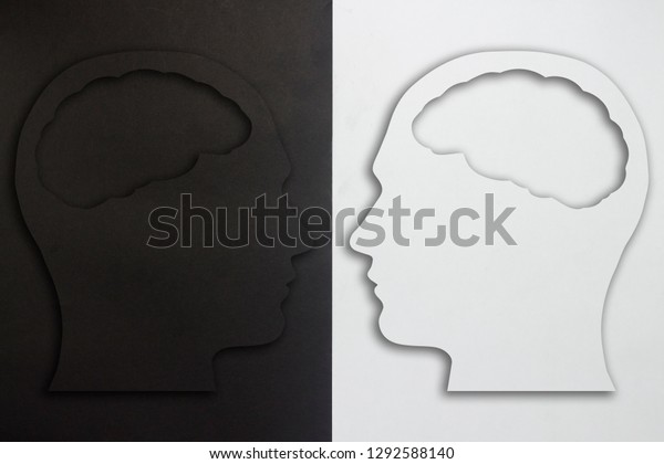 Two paper\
heads with a brain silhouette, black and white on a black and white\
background. The concept of a split personality, different opinions,\
dispute, war. Flat lay, top\
view.