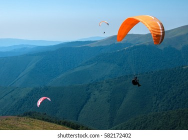 Two paragliders fly over a mountain valley on a sunny summer day. Paragliding in the Carpathians in the summer.