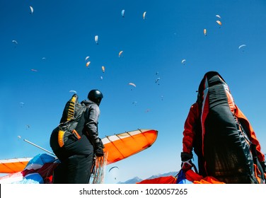 Two paragliders with full flight equipment look on soaring another paragliders in sky