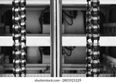Two parallel metal chains hang vertically inside machine. Cylindrical shaft divides frame. Exposed wiring mechanical parts fill background tech industrial technology background