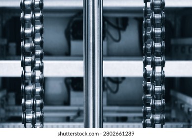 Two parallel metal chains hang vertically inside machine. Cylindrical shaft divides frame. Exposed wiring mechanical parts fill background tech industrial technology background